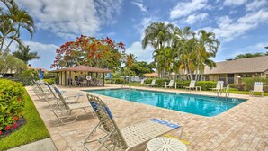 A swimming pool area with lounge chairs, a small pavilion, and palm trees.