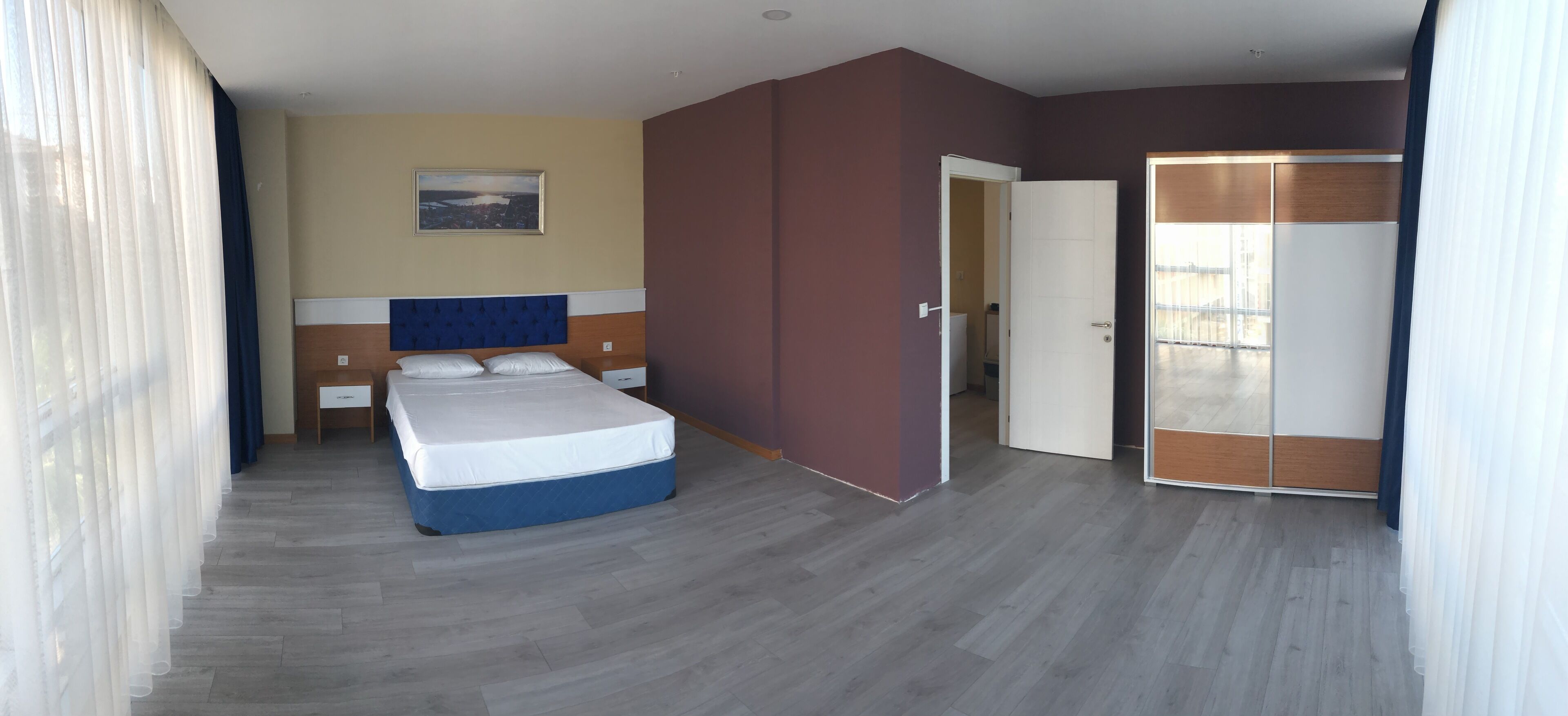 A bedroom with a bed, a nightstand, a wall-mounted TV, and a door leading to another room.