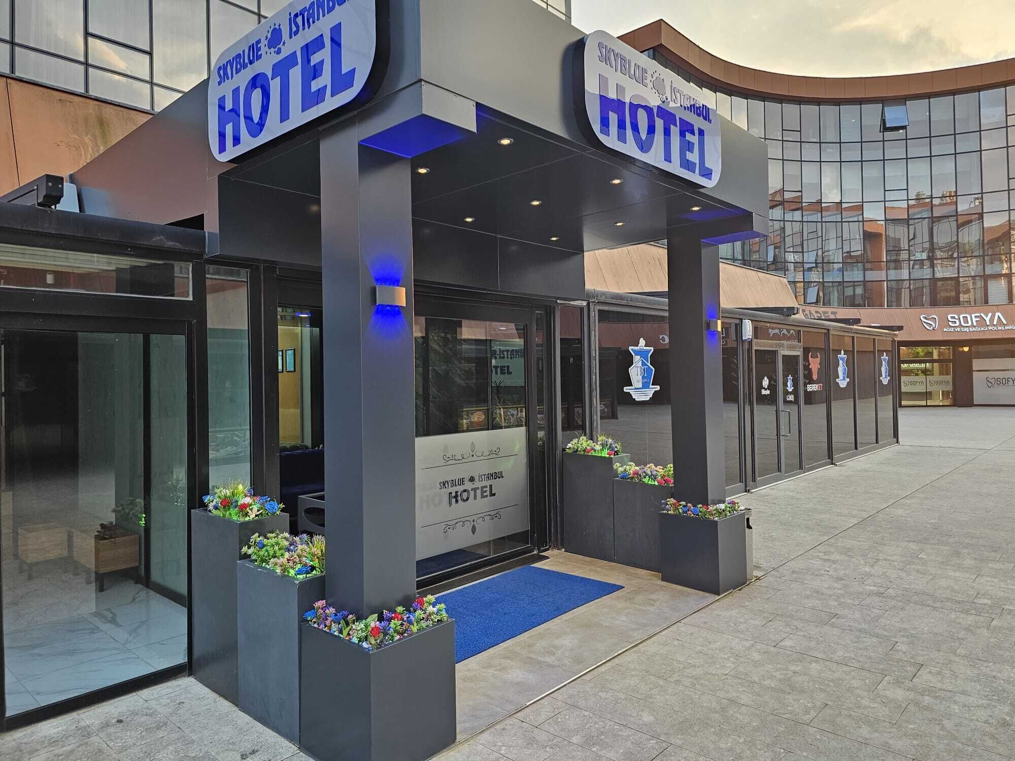 Exterior del Hotel SkyBlue Istanbul, con un diseño moderno, que presenta amplios ventanales y una alfombra azul que conduce a la entrada.