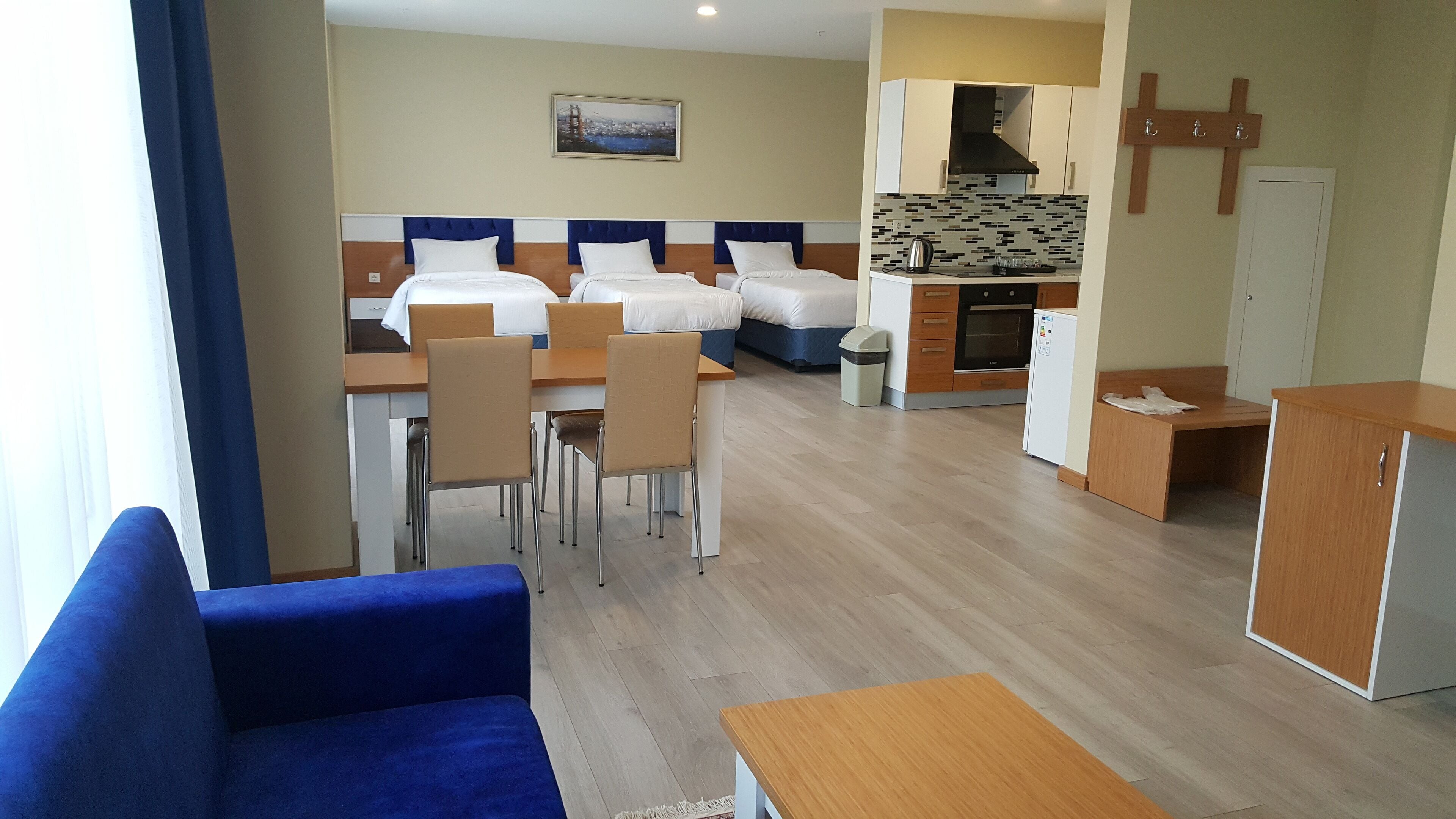 Une chambre d’hôtel avec un lit, un bureau, une chaise, un petit coin cuisine et une croix accrochée au mur.