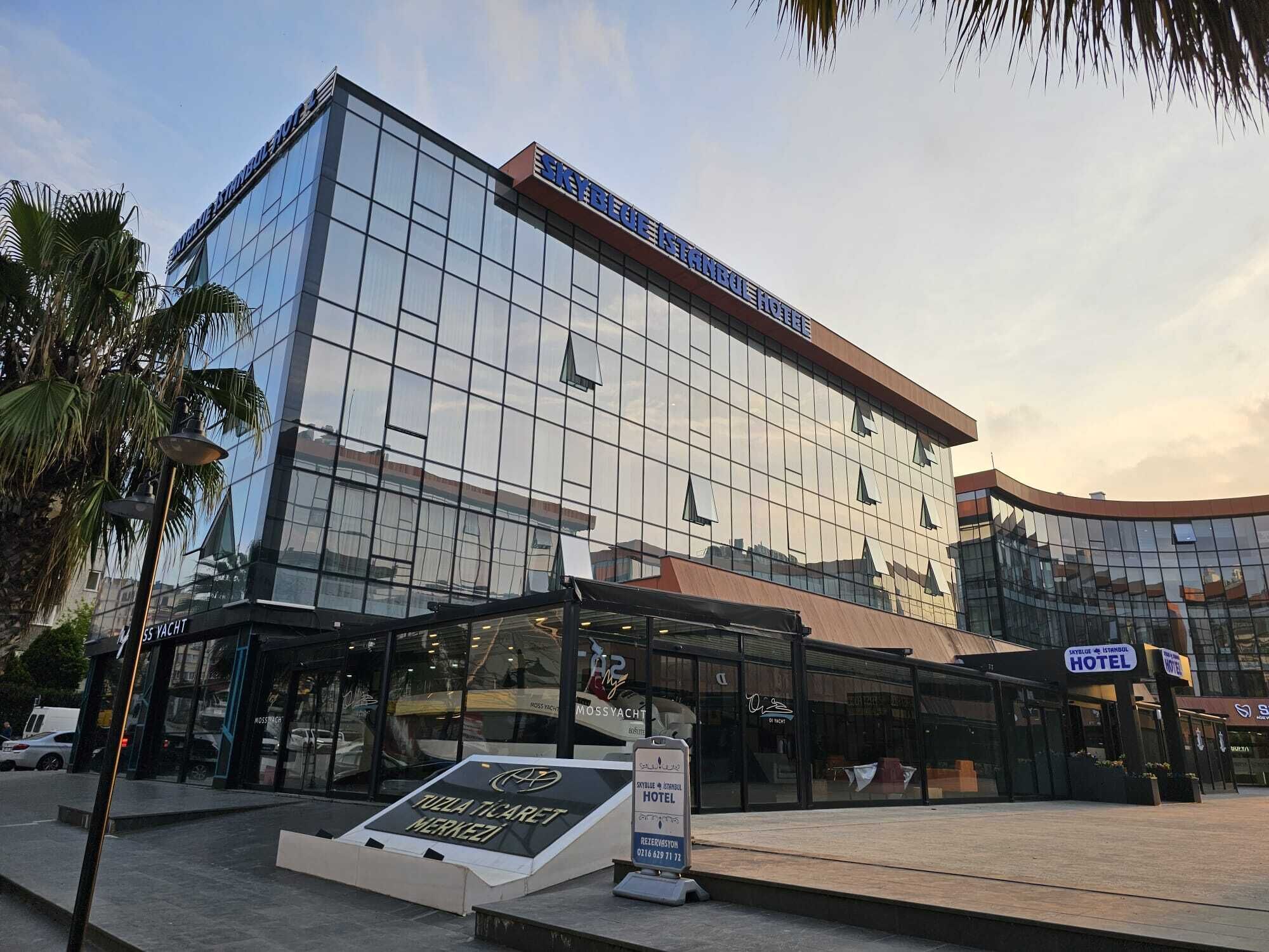 A modern hotel with a glass facade, a covered entrance, and a sign indicating it is a hotel.