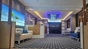 Un vestíbulo de hotel con una zona de estar central, una pantalla grande que muestra una escena de playa y un cartel del Hotel SkyBlue Estambul.