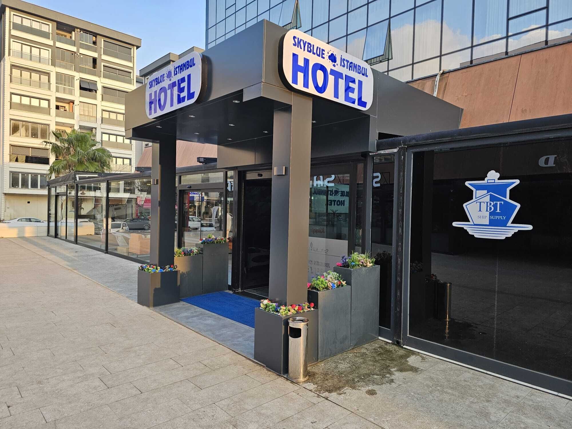 A hotel entrance with a glass canopy, signage for 'Skyblue Istanbul Hotel', and a 'TBT Ship Supply' logo.
