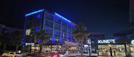 A hotel with a modern glass facade, a visible restaurant, and several parked cars.