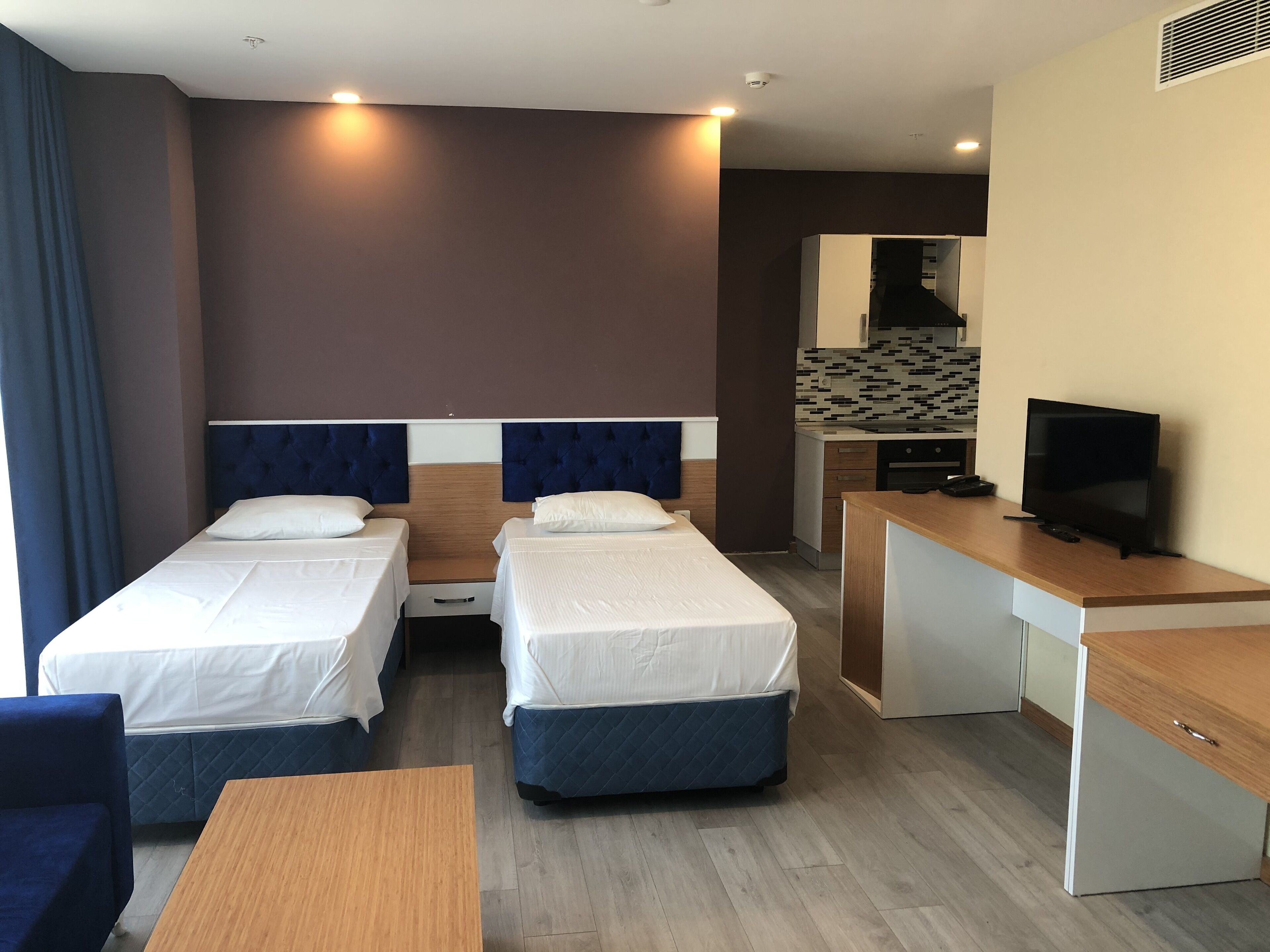 Quarto de hotel com duas camas de solteiro, uma escrivaninha, televisão e cozinha compacta.