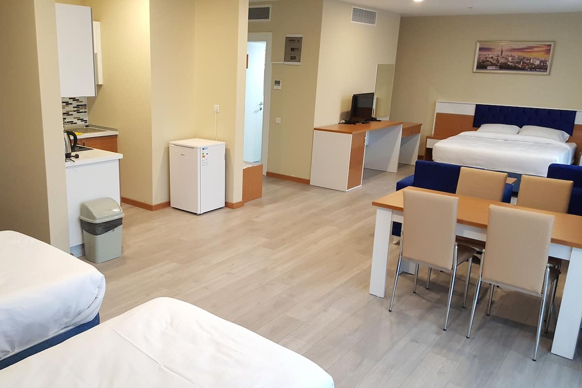 Une chambre d’hôtel avec deux lits, un bureau, une chaise, un petit réfrigérateur et une poubelle.
