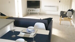 Een moderne woonkamer met een bank, een eettafel voor twee personen, een televisie en een grote wandklok.