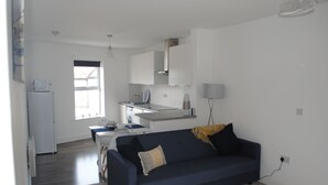 Een moderne woonkamer met een donkerblauwe bank, een kleine tafel en een keuken op de achtergrond.