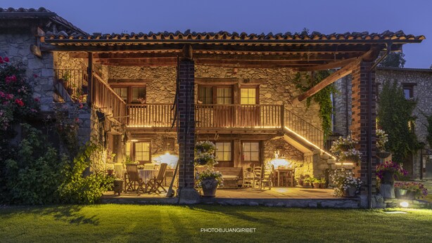 A stone building with a wooden balcony, outdoor seating, and potted plants. - Casa rural cal Rei (Lles)