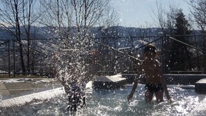 A person in a swimming pool with clear water, surrounded by leafless trees and a metal structure in the background. - Casa rural cal Rei (Lles)