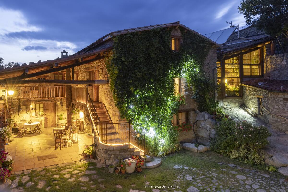 A stone building with a wooden deck, outdoor seating, and a staircase leading to an upper level.