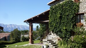 A stone house with a covered porch, a staircase leading to the entrance, and a view of mountains in the background. - Casa rural cal Rei (Lles)