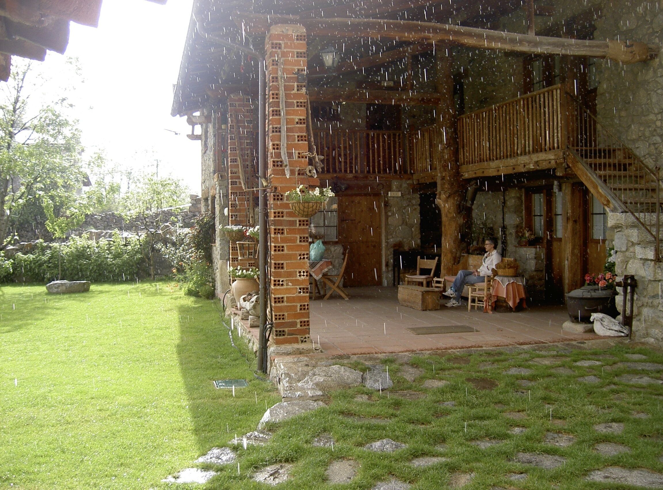 Un edificio rústico de piedra con un balcón de madera, un patio cubierto de césped y un muro de piedra.