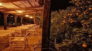An outdoor dining area with wooden tables and chairs, a thatched roof, and a tree with ripe oranges. - Villa near Taormina. (Furci Siculo)