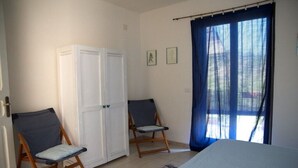 A bedroom with a bed, two chairs, a wardrobe, and a window with curtains. - Villa near Taormina. (Furci Siculo)