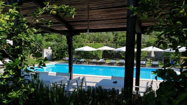 A pool area with lounge chairs and umbrellas, surrounded by greenery. - Villa near Taormina. (Furci Siculo)