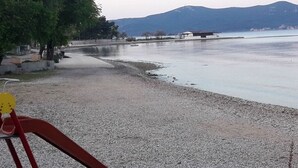 Une plage de galets avec une aire de jeux, un plan d’eau et des montagnes à l’horizon.