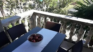 Un balcon avec une table dressée pour deux personnes, un panier de fruits et une vue sur la verdure environnante.