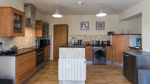 A modern kitchen with wooden cabinets, a built-in oven, a microwave, a washing machine, and a refrigerator. - 80 Kingsway (Bishop Auckland)