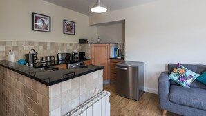 A compact kitchen with a central island, a built-in dishwasher, and a grey sofa with a floral cushion. - 80 Kingsway (Bishop Auckland)