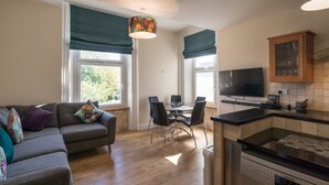 A modern living room with a sofa, dining table, chairs, and a kitchen area with a stove and cabinets. - 80 Kingsway (Bishop Auckland)