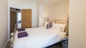 A neatly made bed with white linens and purple towels, a wooden door, and a bedside table with a lamp. - 80 Kingsway (Bishop Auckland)