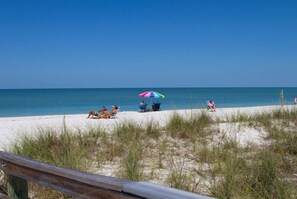 Ein Strand mit Menschen, die unter einem farbenfrohen Sonnenschirm entspannen, mit dem Meer im Hintergrund.