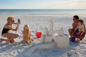 A beach scene with a sandcastle, a child, and an adult.