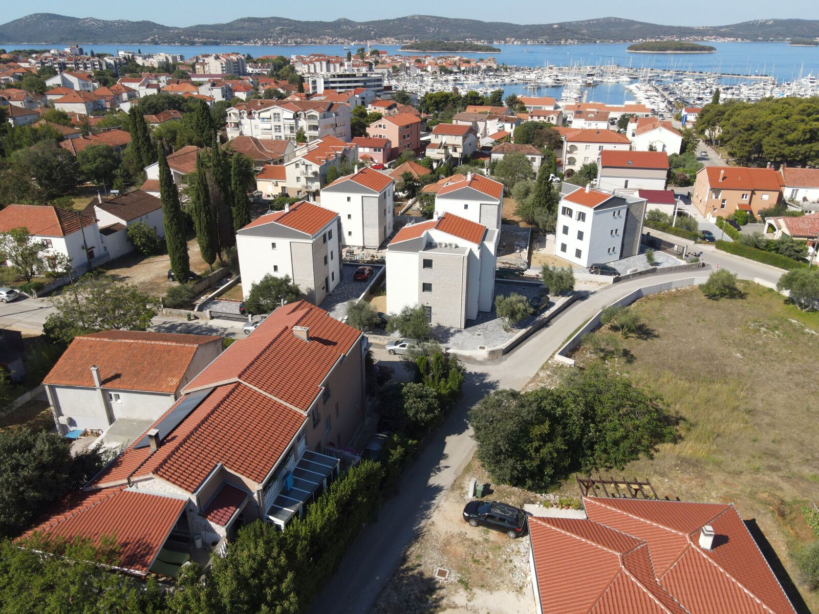 Un quartier résidentiel où les maisons se distinguent par leurs toits recouverts de tuiles rouges et leurs murs blancs, le tout entouré de verdure et bordé d’une marina où sont amarrés des bateaux.