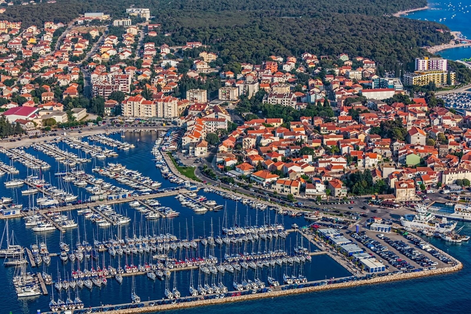 Ett flygbildsbild av en kuststad med en småbåtshamn full av båtar, omgiven av bostadshus med röda tak.