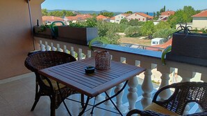Een balkon met rieten stoelen, een houten tafel en uitzicht op huizen en bergen.