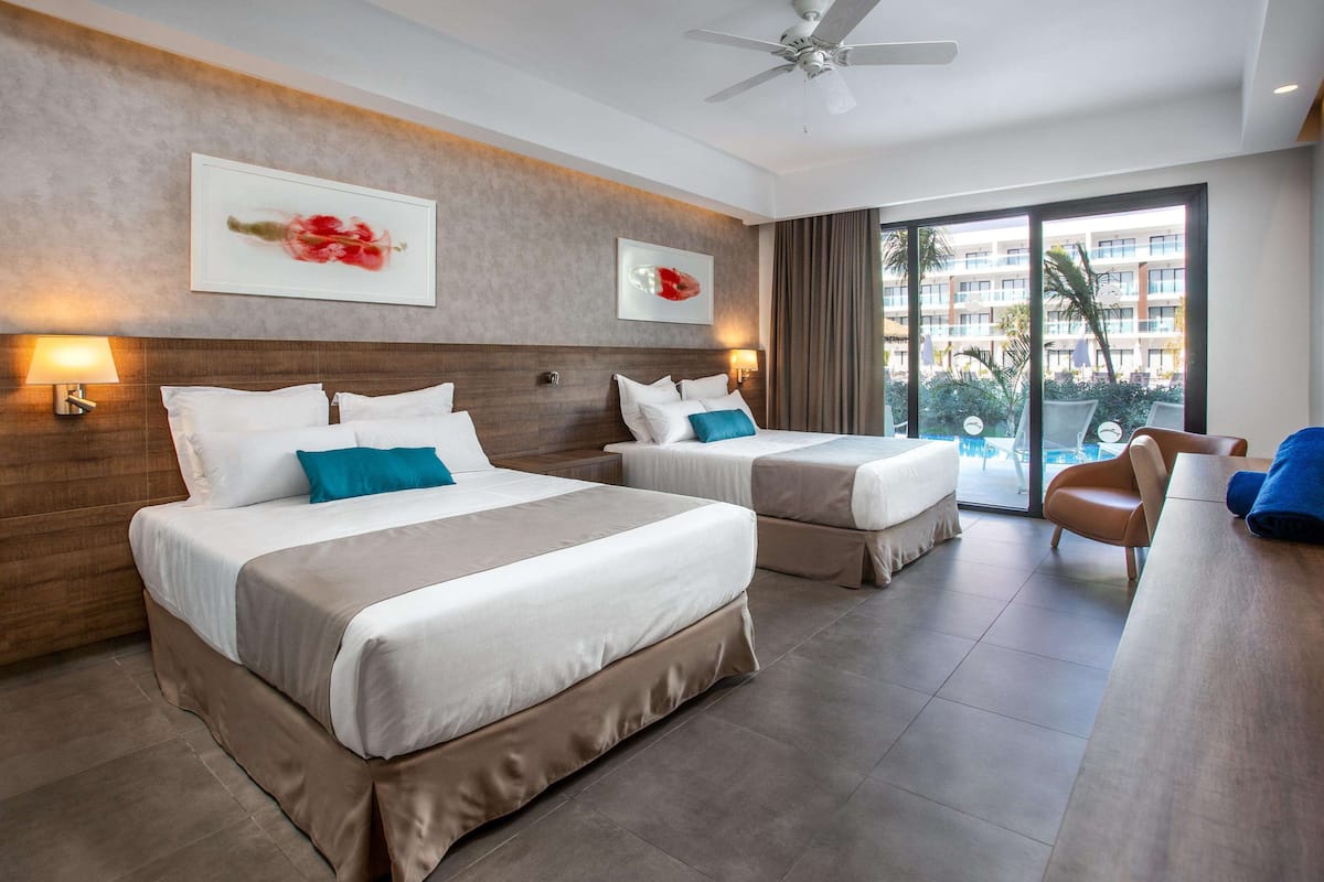 A hotel room with two beds, a ceiling fan, a view of a pool, and a balcony.