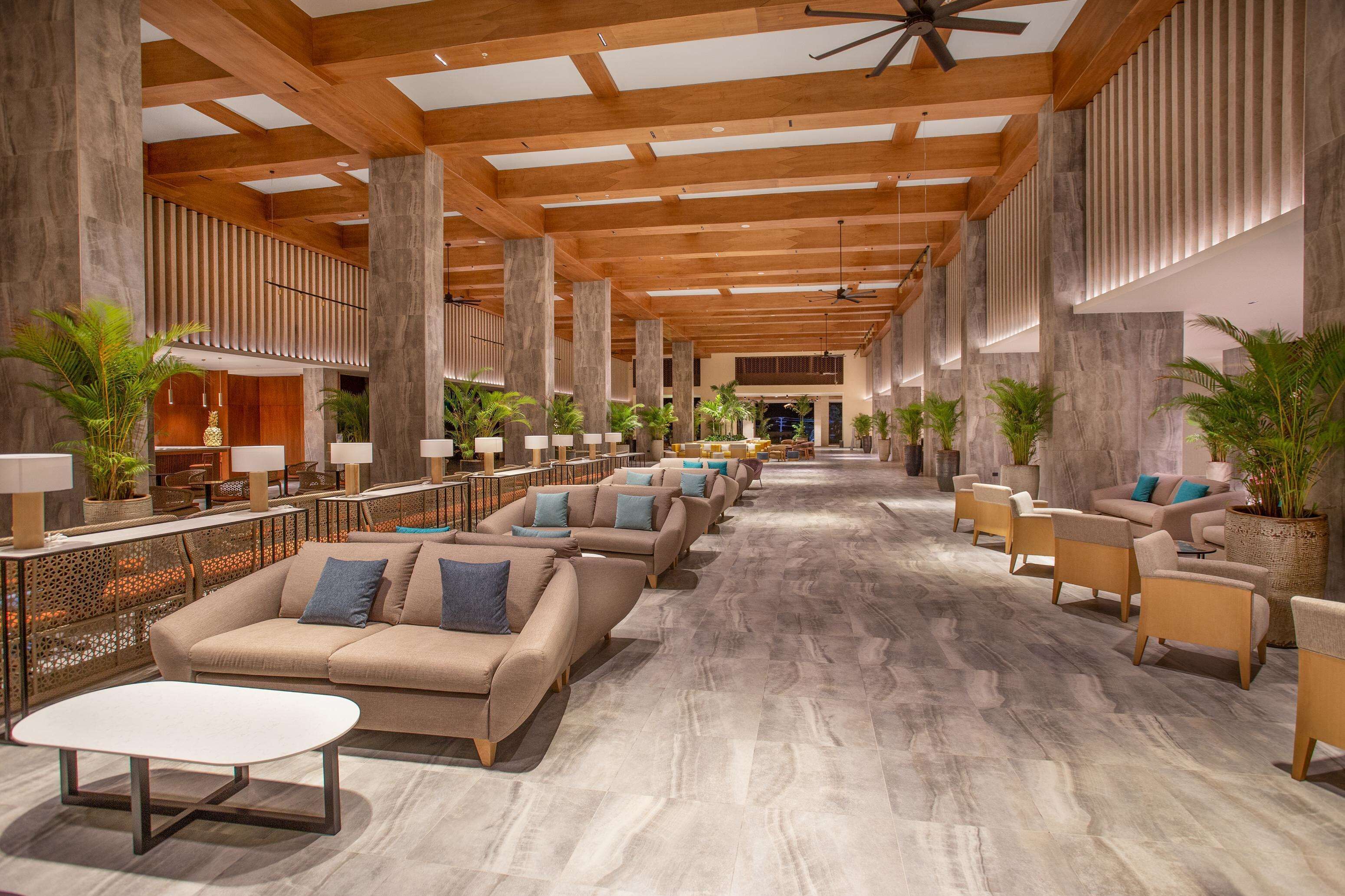 Un vestíbulo amplio con techos altos, vigas de madera y diversas opciones de asientos, incluyendo sofás y sillones.