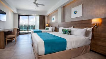 Une chambre d’hôtel avec deux lits, un bureau, une chaise, un ventilateur de plafond et une grande fenêtre donnant sur des immeubles.