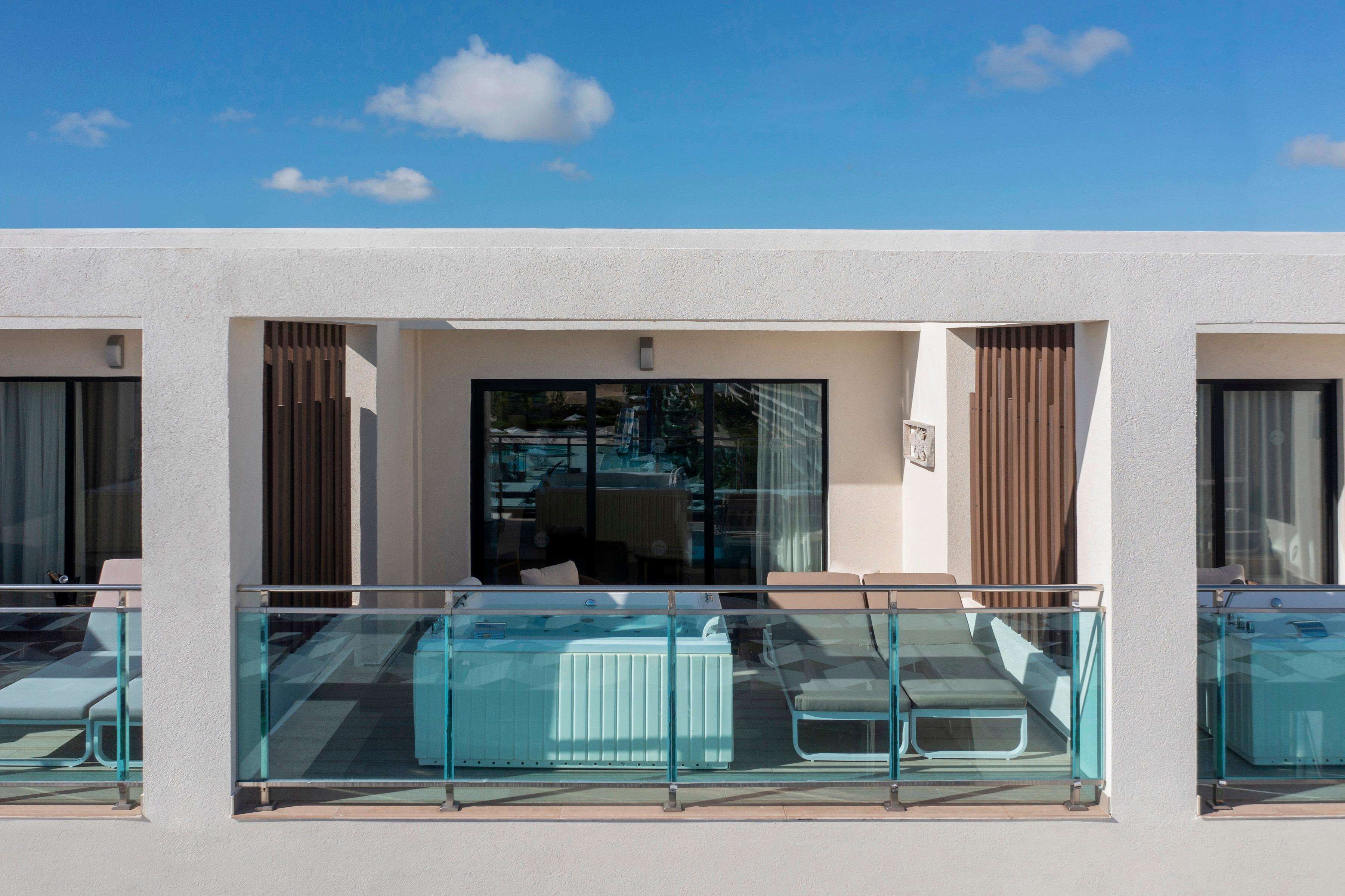 A hotel with a balcony with glass railings, a pool area, and a view of the sky.