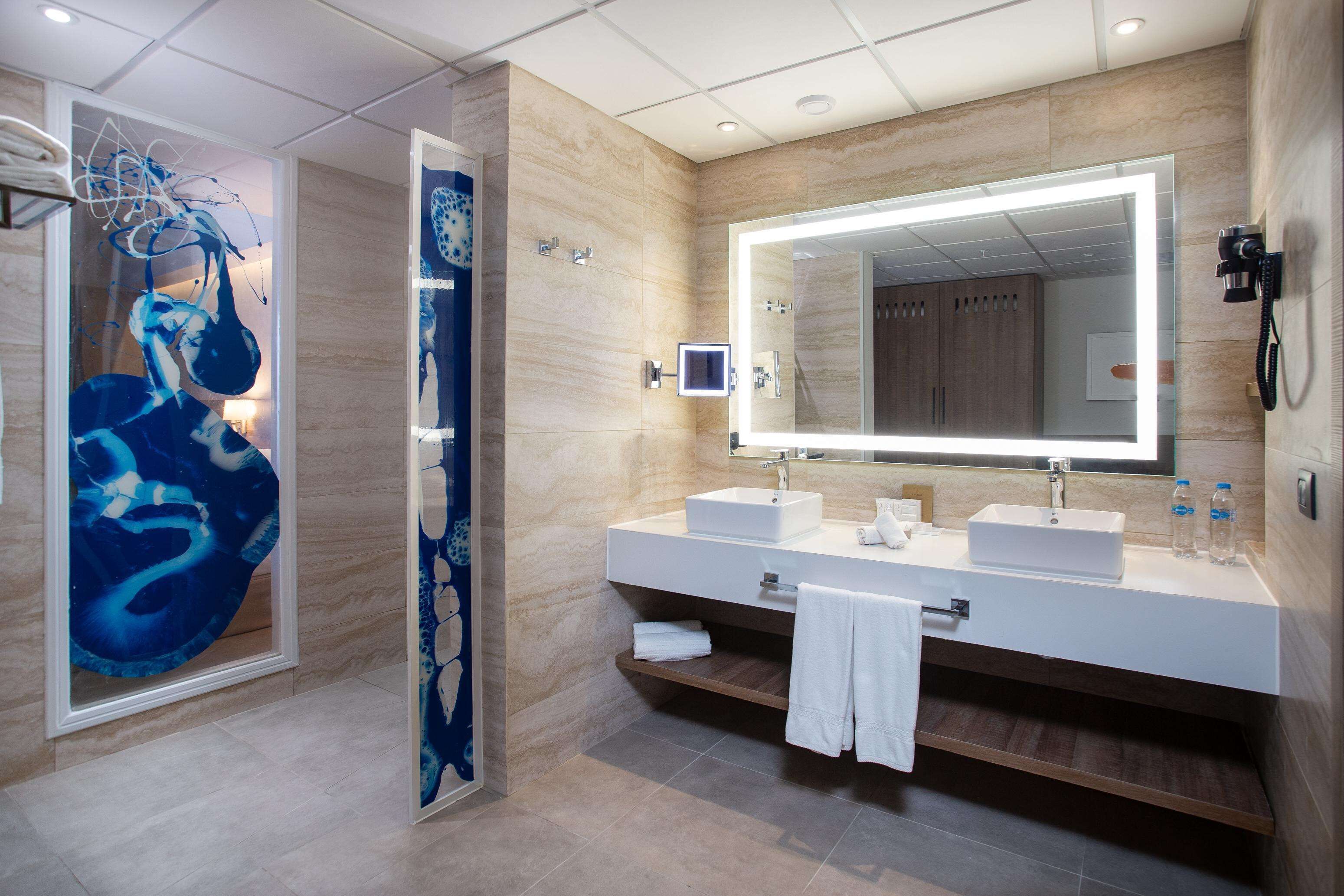 A modern bathroom with a large mirror, two sinks, and a shower area.