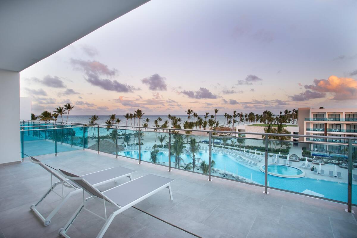 A poolside area with lounge chairs, a glass balustrade, and a view of the pool and palm trees.