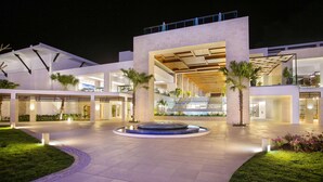 A modern hotel entrance with a central fountain, palm trees, and a well-lit outdoor area. - Serenade Punta Cana Beach & Spa Resort - All Inclusive (Punta Cana)
