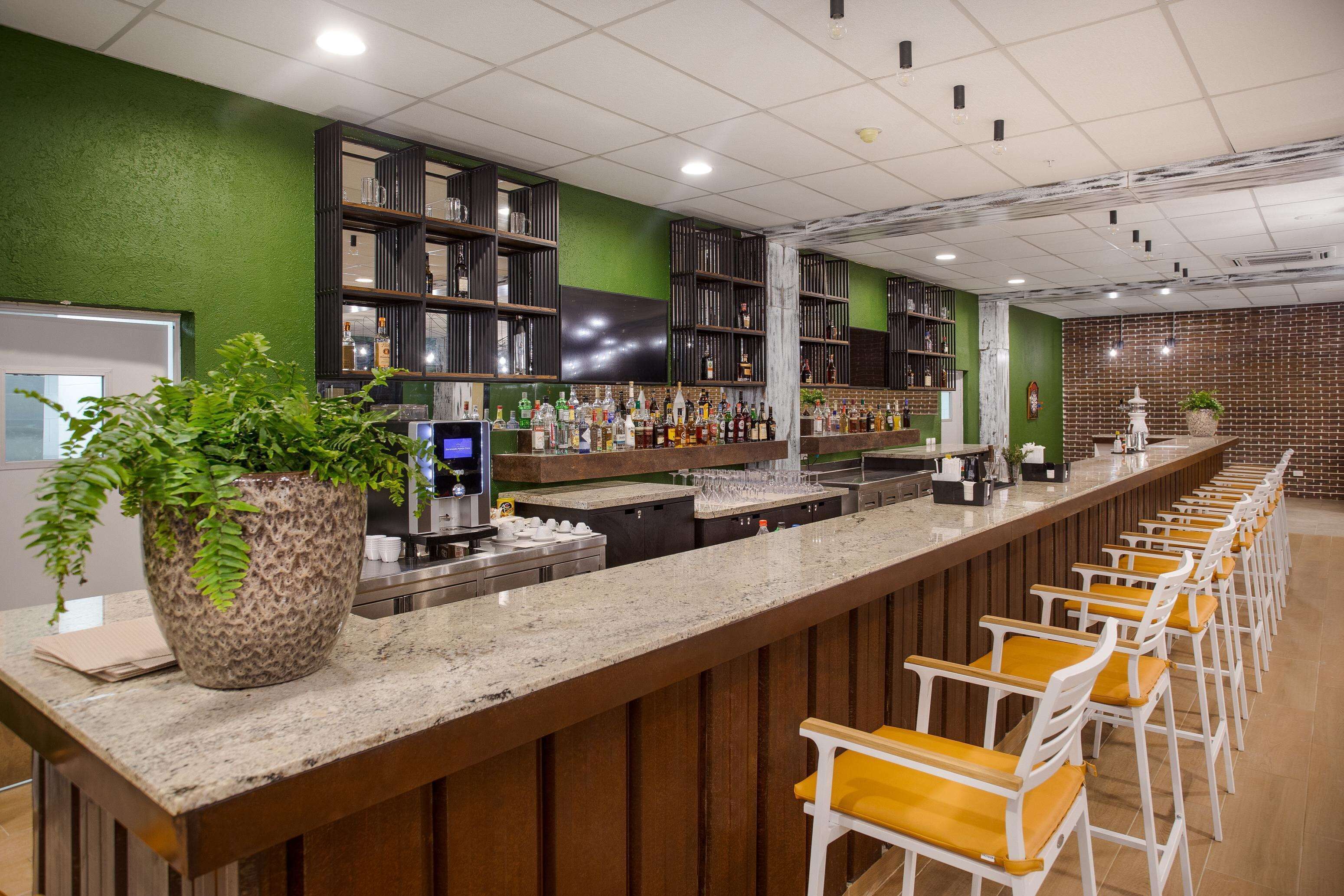 Un'area bar con un lungo bancone, scaffali multipli pieni di bottiglie e diversi sgabelli da bar.