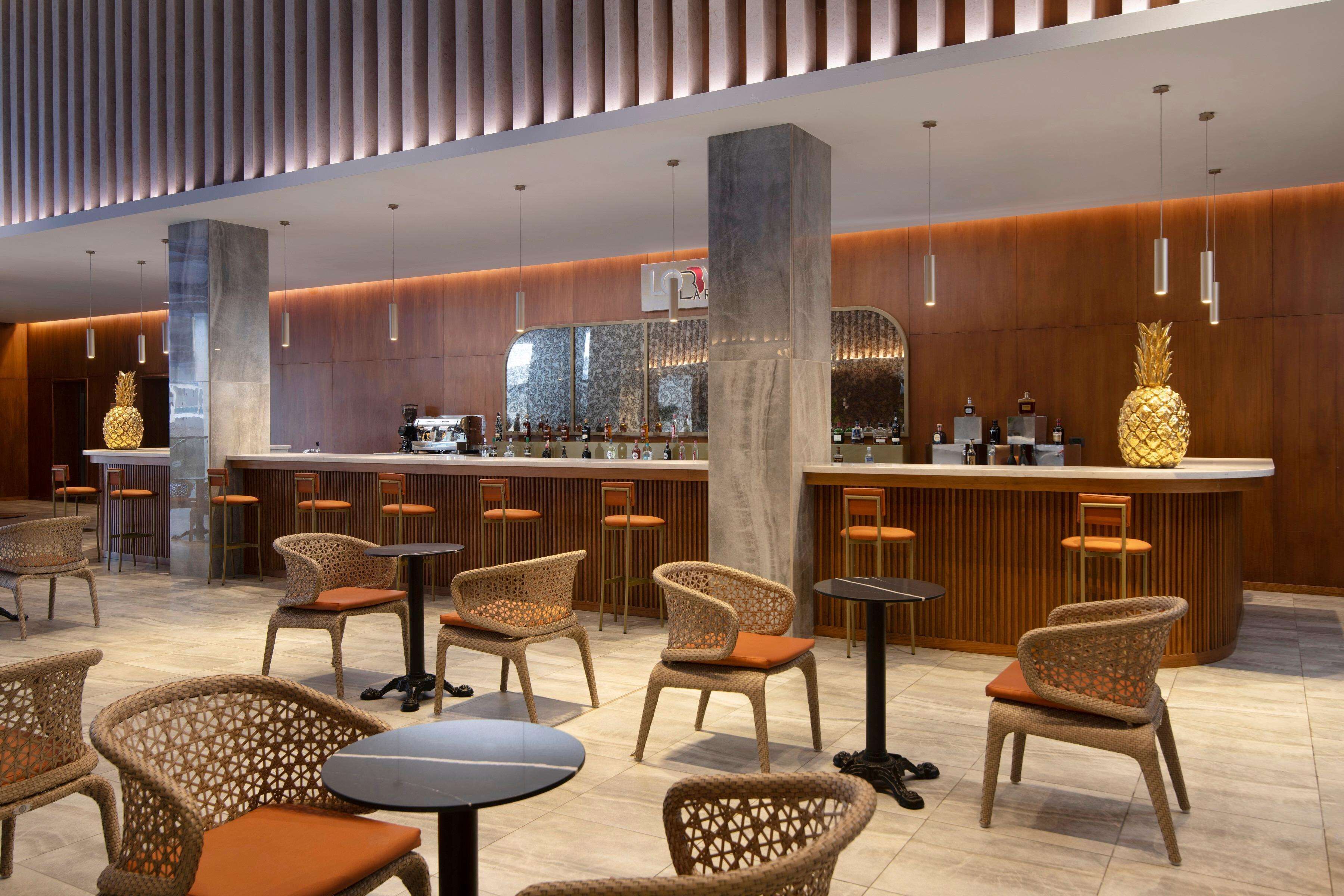 Un espace bar moderne avec des chaises en osier, un comptoir et des luminaires suspendus.