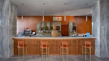 Una zona de bar con un mostrador de madera, tres taburetes y un espejo grande sobre el mostrador.