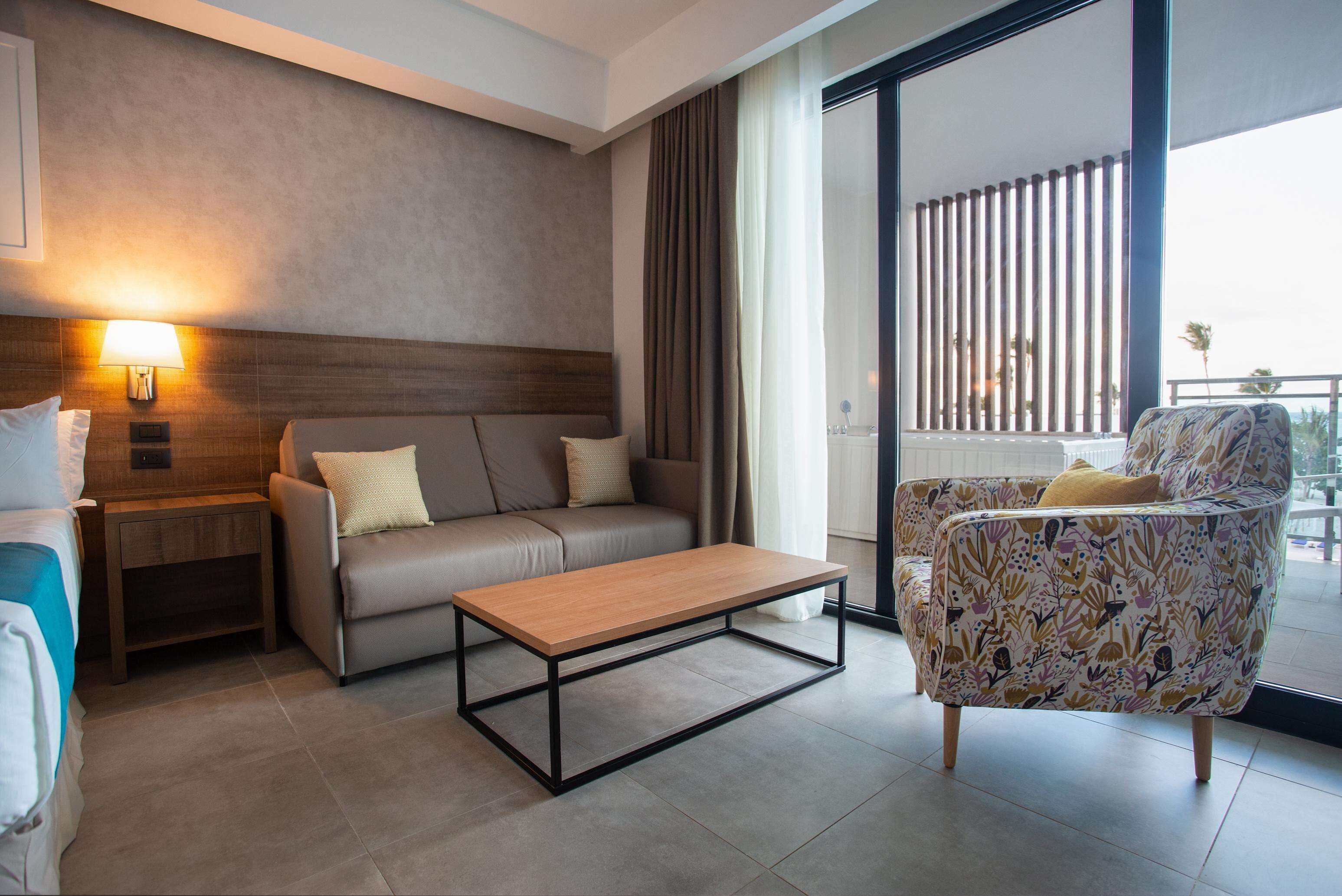 Ein modernes Hotelzimmer mit einer Couch, einem gemusterten Sessel, einem Holztisch, einem Nachttisch und einer Wandlampe.