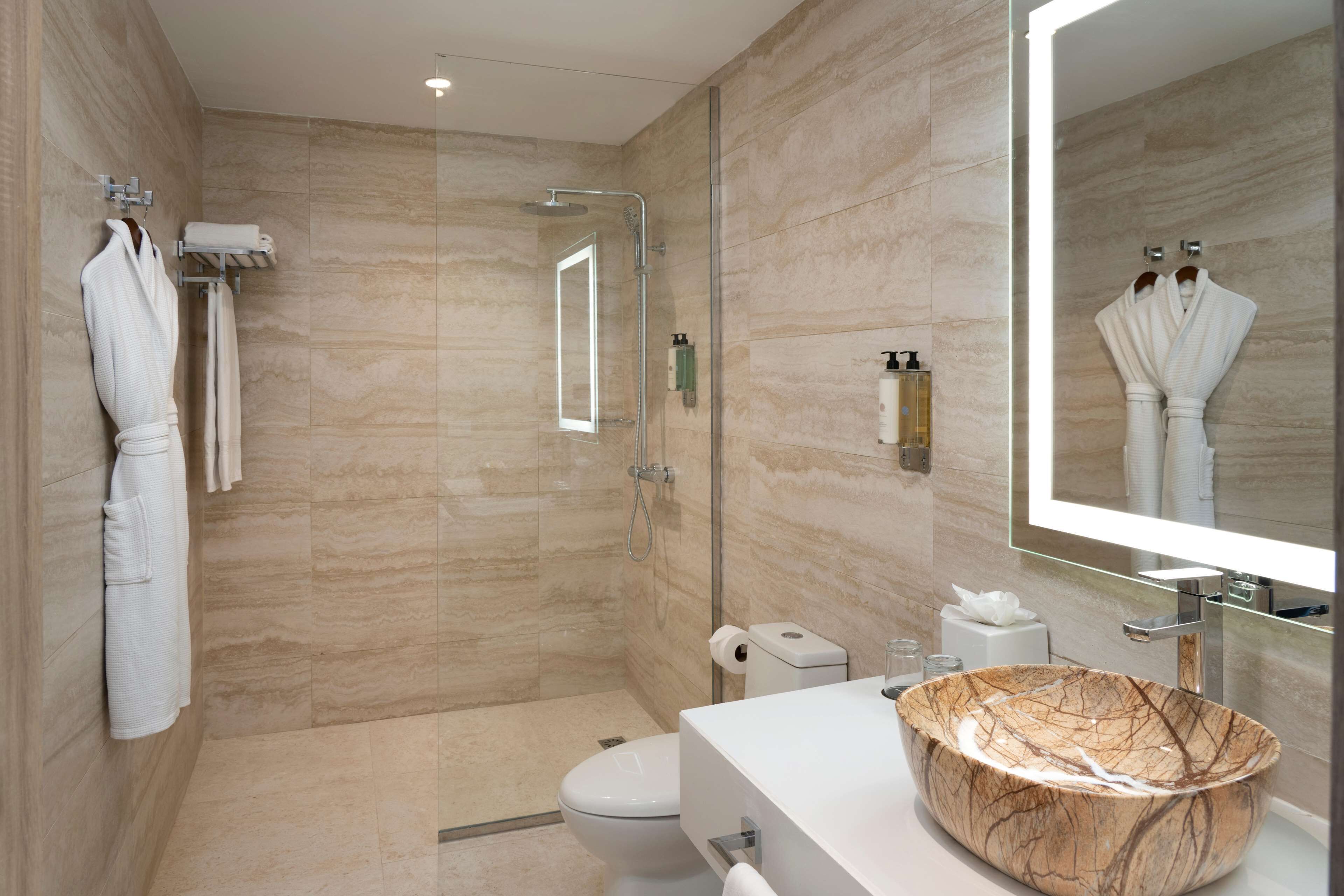 Un baño moderno con ducha envuelta en vidrio, lavamanos de mármol y un espejo grande.