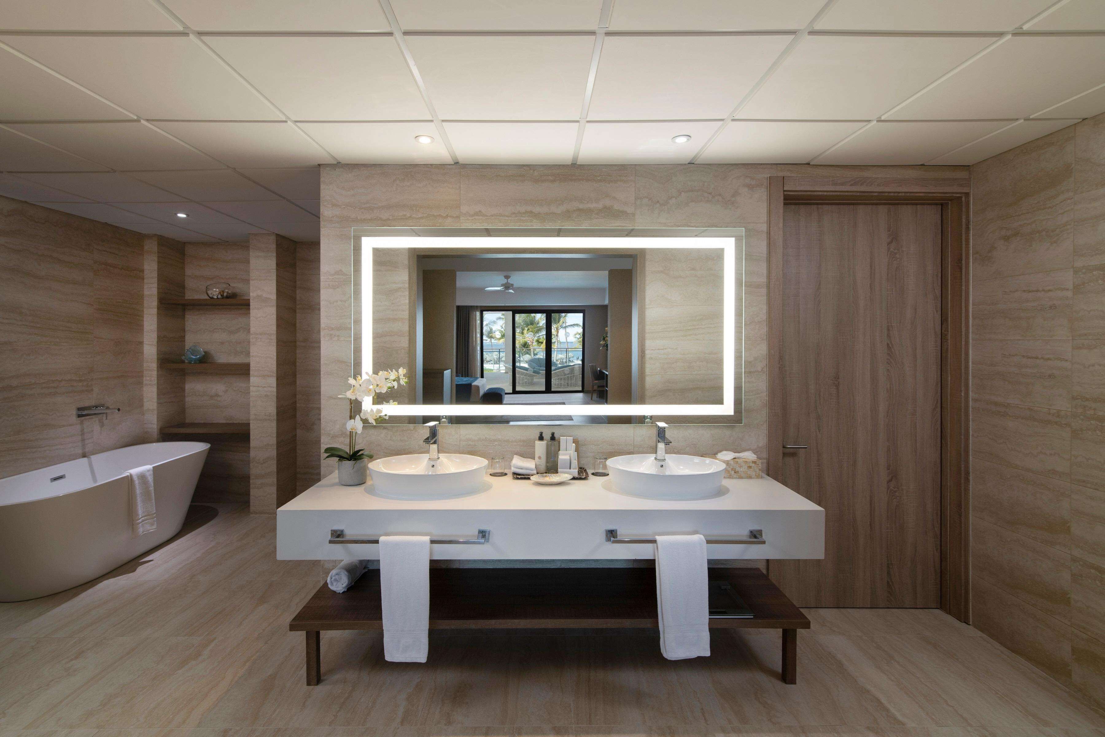 Un bagno moderno con due lavabi, uno specchio grande e una vasca da bagno indipendente.