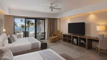 Hotelkamer met een groot bed, een televisie, een zithoek met een stoel en uitzicht op het strand.