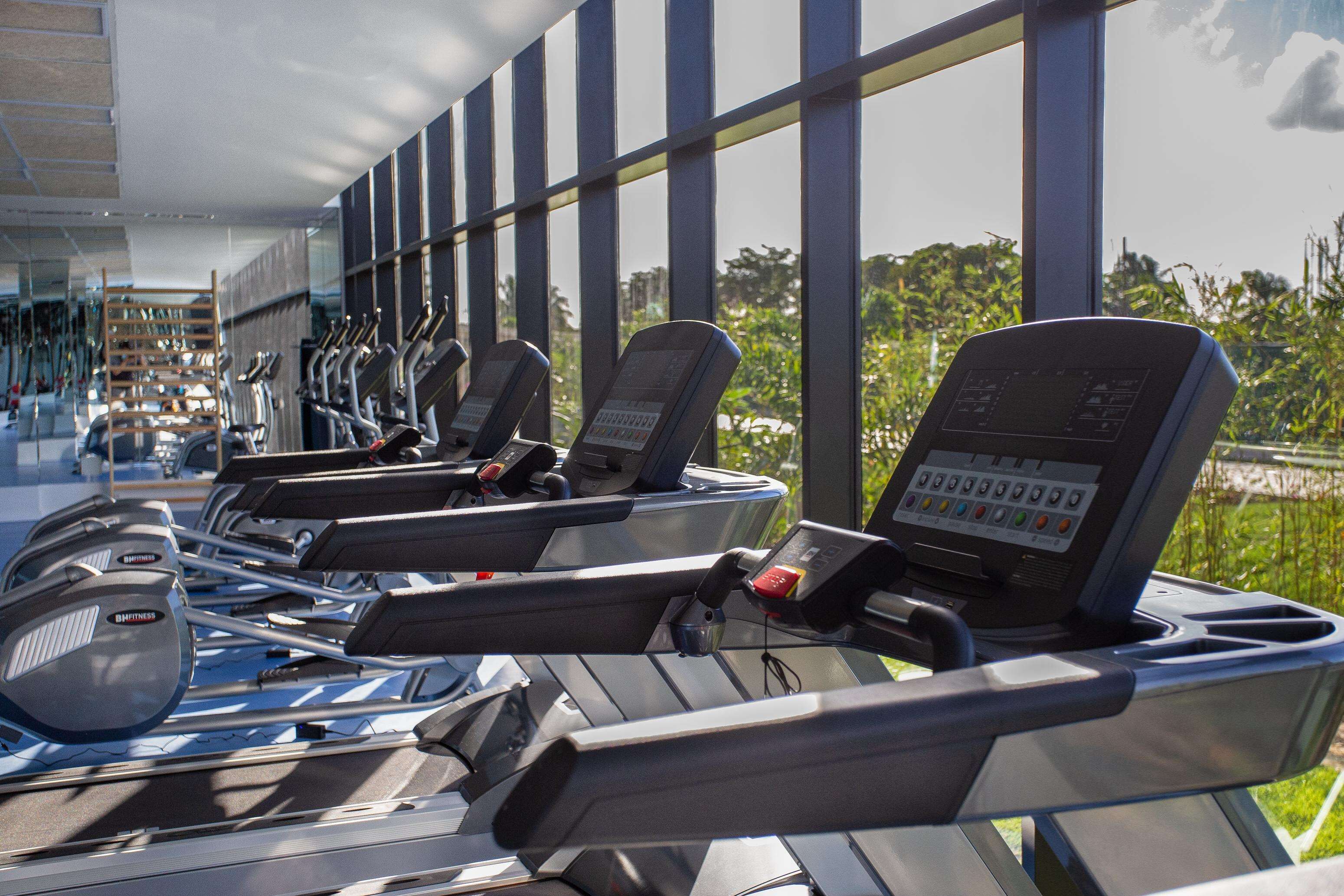 Une rangée de tapis de course dans un centre de remise en forme moderne, doté de grandes fenêtres offrant une vue sur la verdure.