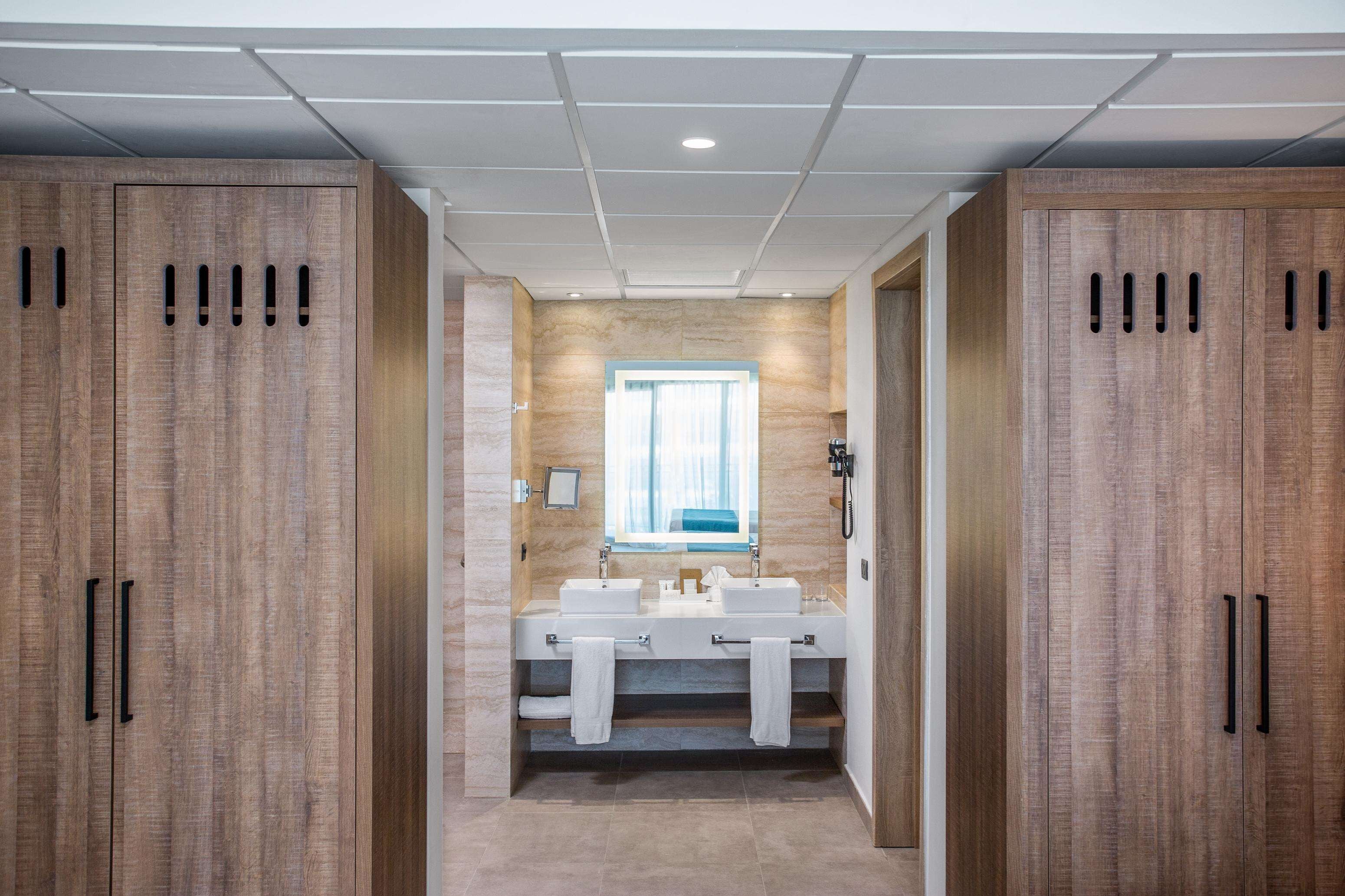 Un baño moderno con armarios de madera, un tocador con doble lavabo y un espejo grande.