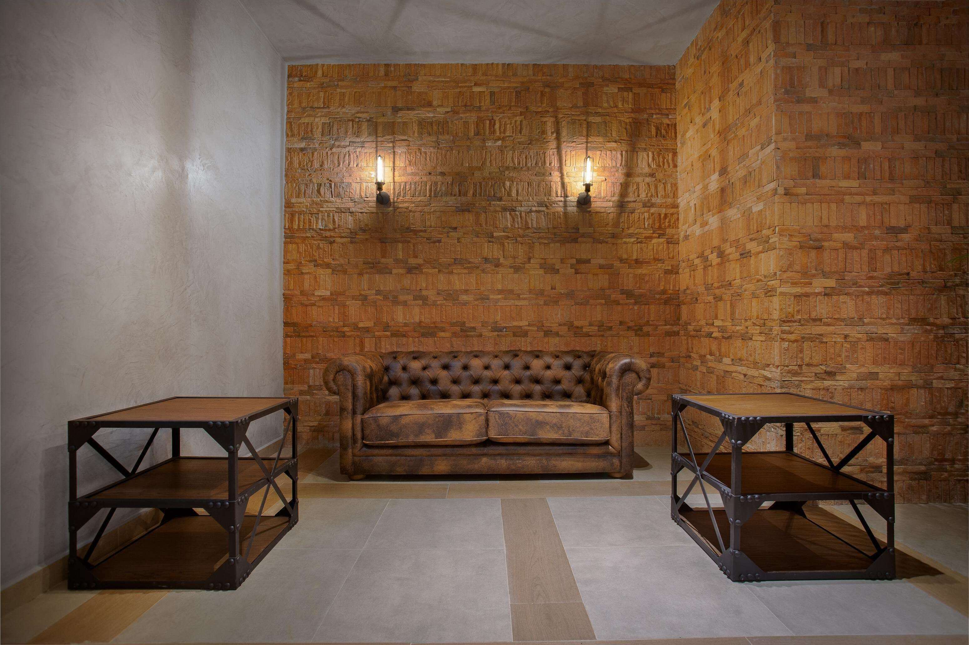 A room with a brown leather sofa, two metal tables, and a brick-patterned wall.