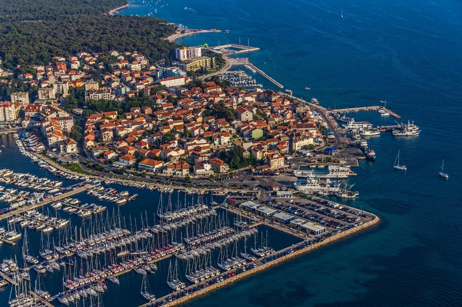 An aerial view of a coastal town with a marina filled with boats, surrounded by residential buildings and a prominent lighthouse.