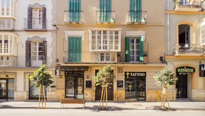 Un edificio con varios balcones, una tienda con un estudio de tatuajes y un banco en la entrada.